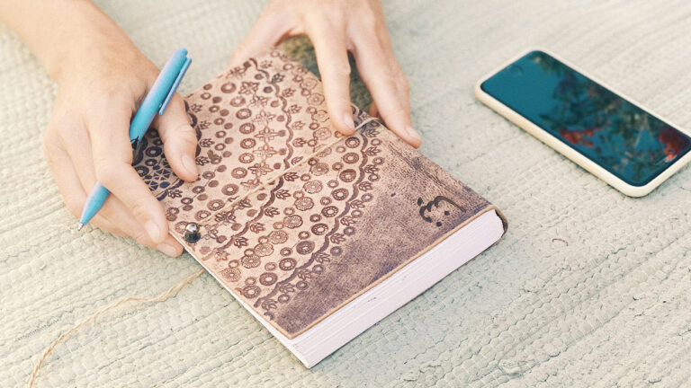 Nina Raem mit einem Notizbuch und Stift in der Hand, Mobiltelefon daneben liegend notiert ihren Yoga Stundenplan