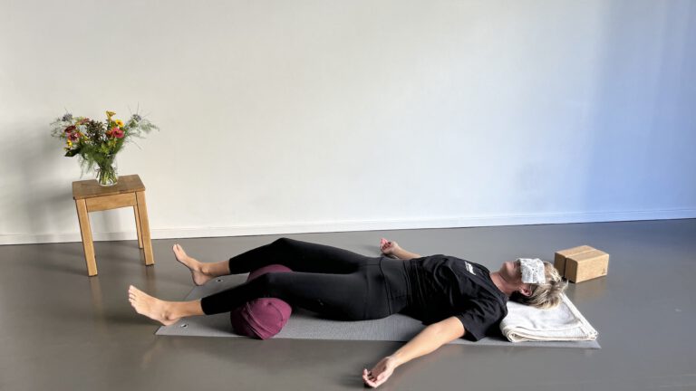 Position für Yoga Nidra mit Hilfsmitteln wie Bolster für die Kniebeugen, Decke unter dem Kopf und Augenkissen