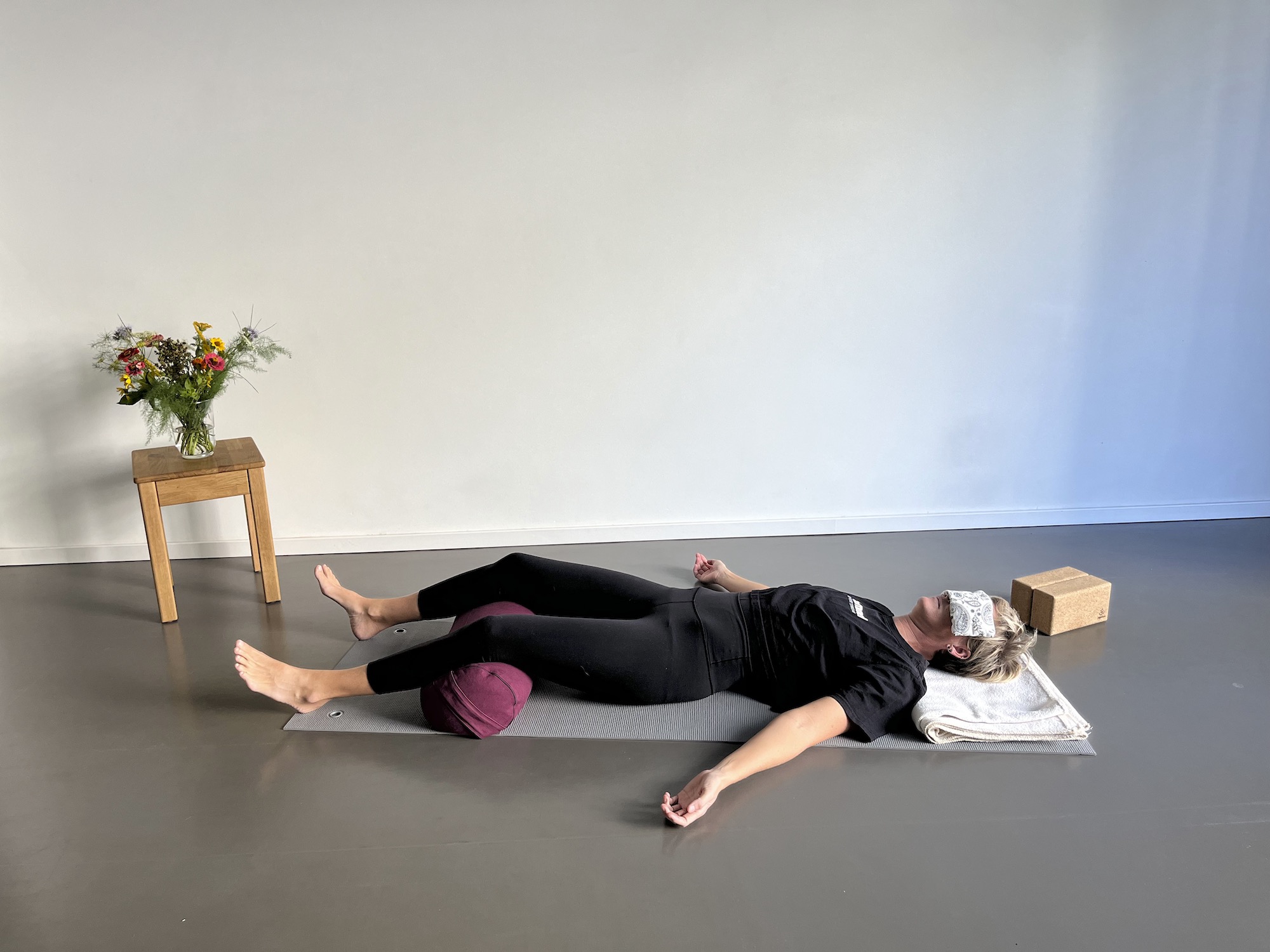 Position für Yoga Nidra mit Hilfsmitteln wie Bolster für die Kniebeugen, Decke unter dem Kopf und Augenkissen